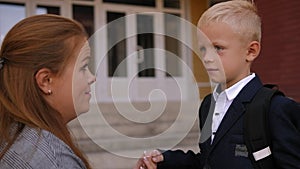 A caring mother straightens her son's jacket on the school stairs near the door.