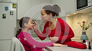 Caring mother teaching daughter putting on makeup on face skin indoors