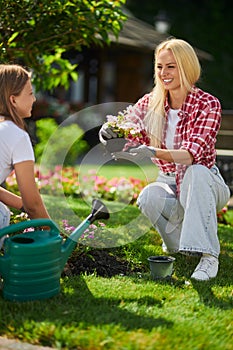 Caring mother teaching daughter to plant flowers at garden