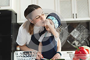 Caring mother teaching little daughter to cook salad in kitchen, young mum and adorable cute girl child wearing apron