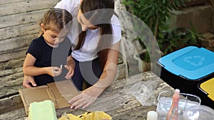 Caring about nature. Young mom with her little daughter preparing for recycling different kind of rubbish and putting