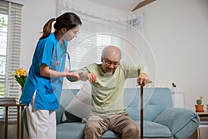 Caring nurse helping supporting senior disabled man to stand up with walking stick