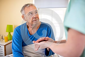 Caring nurse holding a hand of a senior man occupant in a nursing home room