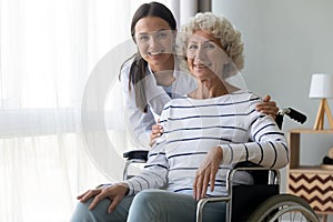 Caring nurse hug elderly disabled woman in wheelchair posing indoors photo