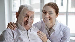 Caring nurse hugs old man patient smiling looking at camera