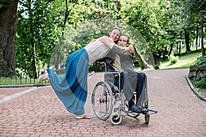 Caring nurse or social worker, pretty young hipster girl walking in park with senior man patient sitting on wheelchair