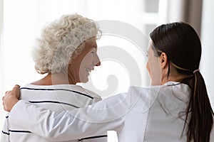 Caring nurse supporting hugging elderly woman clinic patient rear view