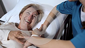 Caring nurse telling jokes to old female patient lying in sickbed rehabilitation photo