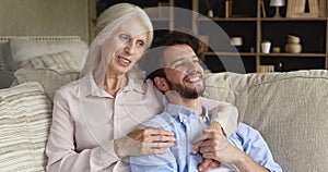 Caring old mother cuddle adult son talk to young man