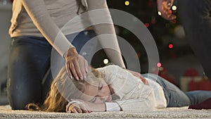 Caring parents stroking little daughter sleeping near X-mas tree cant wait gifts