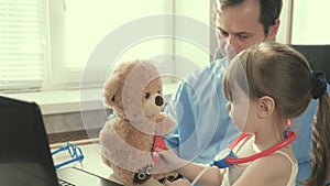 Caring professional male pediatrician playing with a small child in the office. little girl plays with teddy bear toy