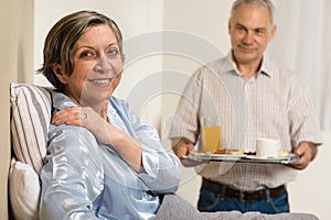 Caring senior man bringing breakfast to wife