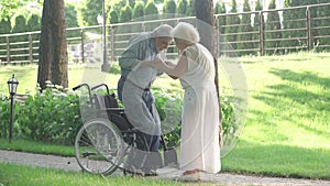 Caring senior woman helping handicapped man to stand up from wheelchair and walk. Thankful Caucasian husband hugging