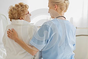 Volunteer sitting on a hospice bed next to an senior resident and strokes her back photo