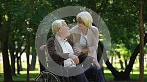 Caring woman supporting her husband in wheelchair, kissing each other, family