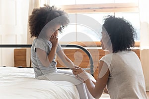 Worried african mother holding hand comforting sad little daughter photo