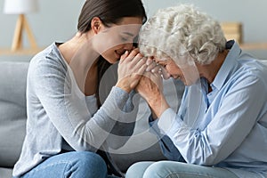 Caring young adult woman granddaughter hold hands of old grandmother