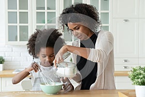 Caring young african american mother helping little daughter with bakery.