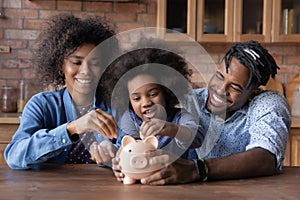 Caring young African American parents teaching small daughter saving money,