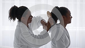 Caring young african american woman combing hair of her beautiful teen sister