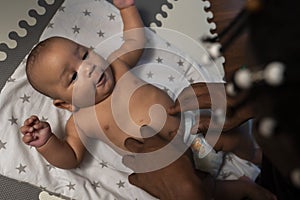 Caring young black father tickling tummy of his newborn baby . Fatherhood and multiracial family photo