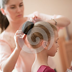 Caring young caucasian mother woman fixing her little beautiful thin girl daughter hair bun