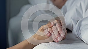 Caring young hand holding the hand of an old and sick loved one. Love, compassion and family support. Close-up.