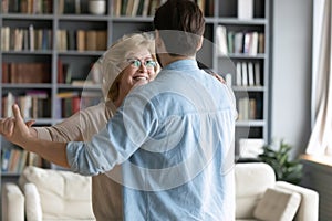 Caring young man leading in dance smiling 60s mother.