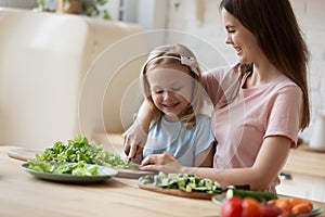 Caring young mom teach little daughter chop vegetables