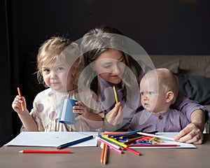 Caring young mom teaching how to draw her two little kids