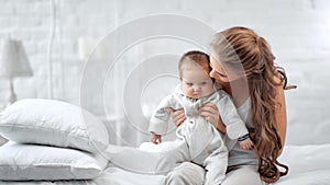 Caring young mother playing with little cute baby enjoying motherhood at morning bedroom