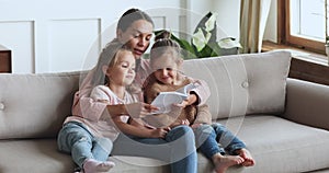 Caring young mother reading book hug cute children daughters