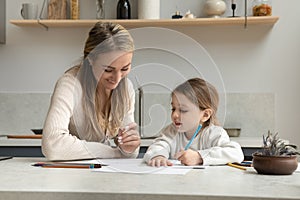 Caring young 35s woman teaching small girl writing letters. photo