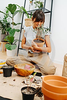 Caring young woman in living room looking dearly at the plant in her embrace