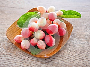 Carissa carandas or karonda are white and red with green leaves in wooden plates. On the old wood table It is a small fruit