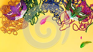 Carnaval accessories flat lay on bright yellow background, top view, copy space. Frame with traditional Mardi gras beads, masks,