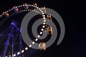 Carnival entertainment Ferris wheel motion with dark blue illumination from frame and yellow from cabins at night time black sky