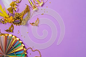 Carnival or mardi gras concept with golden carnival masks and party decorations on purple background. Top view, flat lay