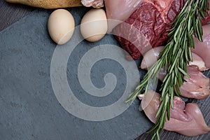 Carnivore keto diet flat lay. eggs, beef steak, chicken breast and pork shank assorted meat near a board made of natural stone.