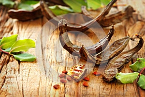 Carob. Healthy organic sweet carob pods with seeds and leaves on a wooden table. Healthy eating