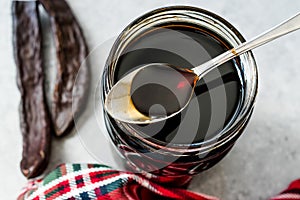 Carob Molasses Dripping from Spoon to Jar