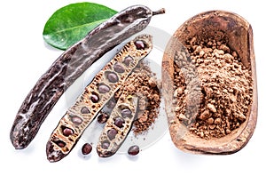 Carob pods and carob powder in the wooden bowl