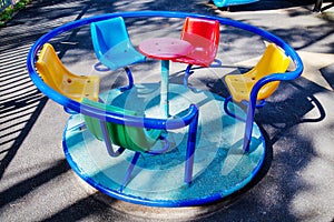 The carousel is metal with plastic chairs of red green yellow color on the playground with a rubberized coating.