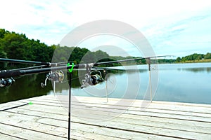 Carp fishing on beautiful blue lake with carp rods and rod pods in the summer morning. Fishing from the wooden platform