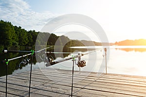 Carp fishing on beautiful blue lake with carp rods and rod pods in the summer morning. Fishing from the wooden platform