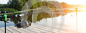 Carp fishing on beautiful blue lake with carp rods and rod pods in the summer morning. Fishing from the wooden platform.