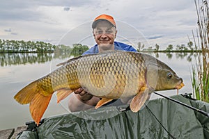 Carp fishing. Fisherman with fish trophy in hands at lake