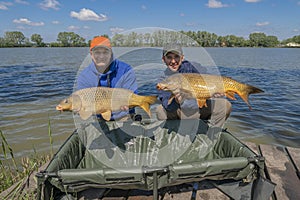 Carp fishing. Two fisherman with fish trophy in hands at lake