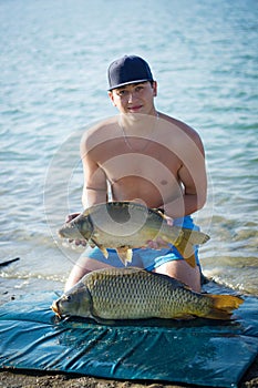 Carp fishing. Young smiling fisherman with two common carps.