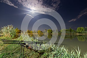 Carp spinning reel angling rods on pod standing. Night Fishing, Carp Rods, Cloudscape Full moon over lake.